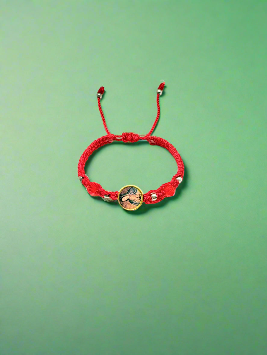 Red woven baby bracelet with Our Lady of Guadalupe charm, silver beads, and adjustable cord for infants aged 0–12 months on a white background a green background