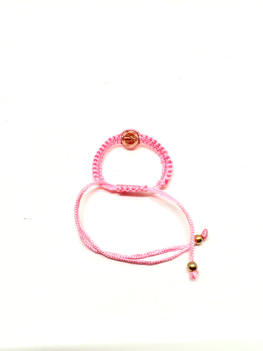 Back view of pink St. Benedict baby bracelet braided bracelet with a circular St. Benedict medal charm on a white background.