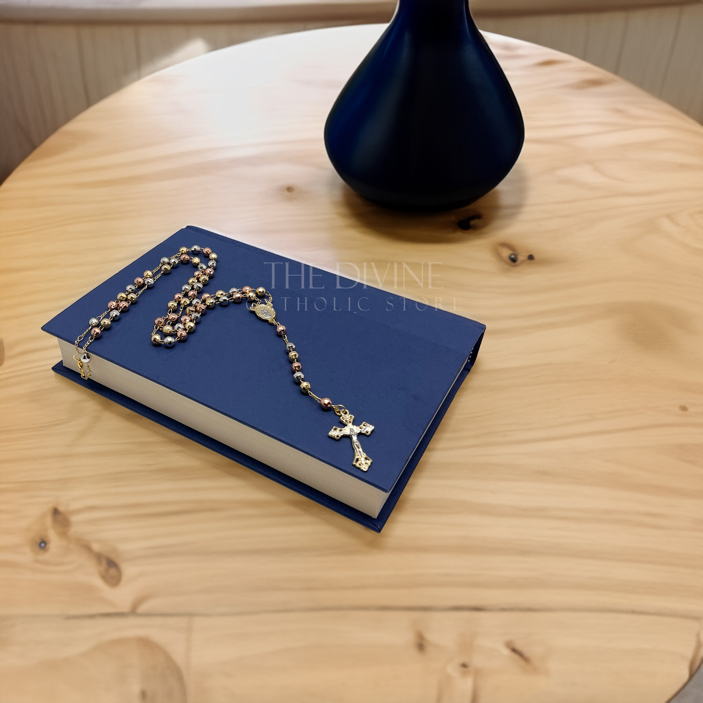 Elegant 18k gold plated rosary prayer beads with Our Lady of Guadalupe centerpiece sitting on a blue book sitting on a table next to a black lamp.