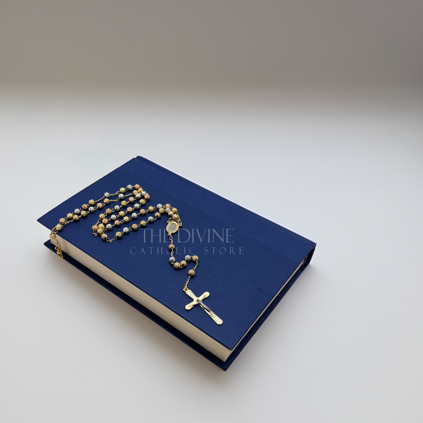 Elegant 18k gold plated rosary prayer beads with Our Lady of Guadalupe centerpiece sitting on a blue book and white background.