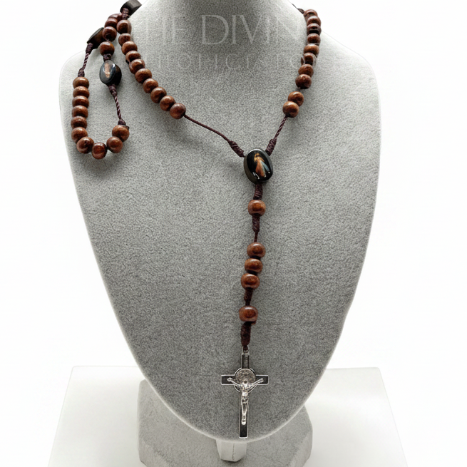 Divine Mercy wooden rosary displayed on gray jewelry bust, 17-inch Catholic prayer beads with St. Benedict crucifix on a white table top and white background surrounded by green plants.
