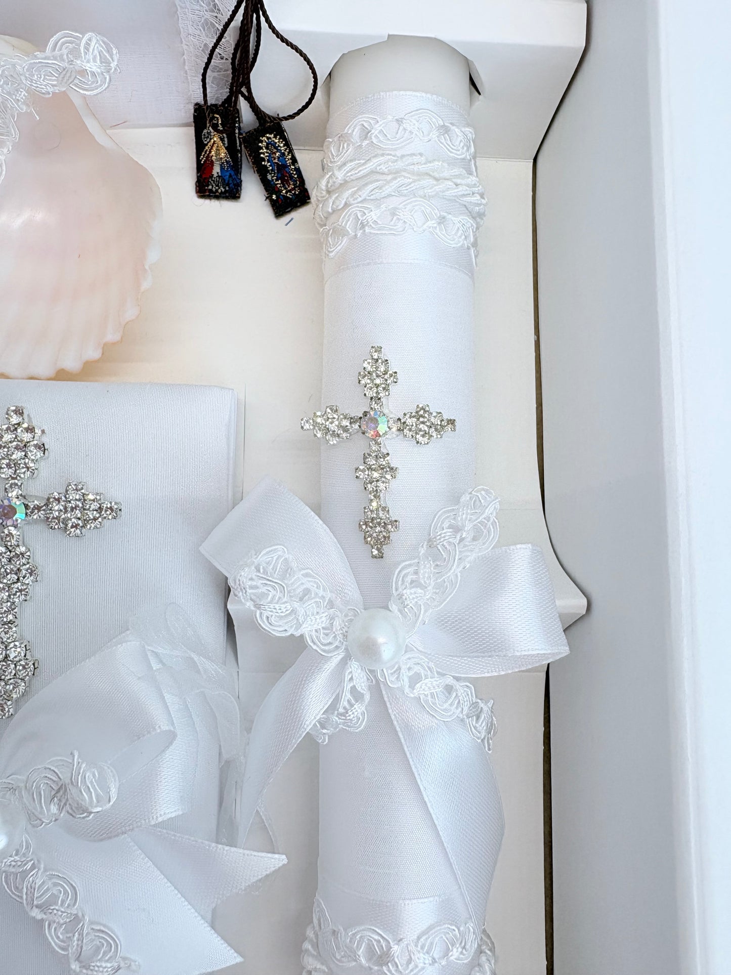 Closeup of sparkling rhinestone cross brooch with aurora borealis crystal center on white baptism candle with pearl bow