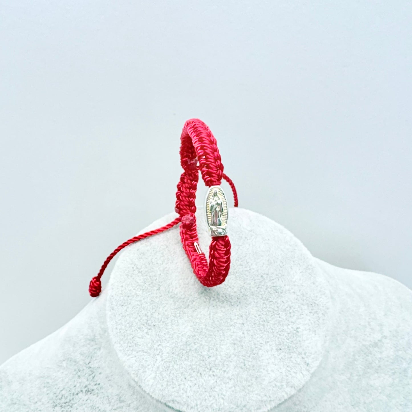 Red adjustable baby bracelet with Our Lady of Guadalupe medal shown upright on display stand, Catholic infant jewelry detail view