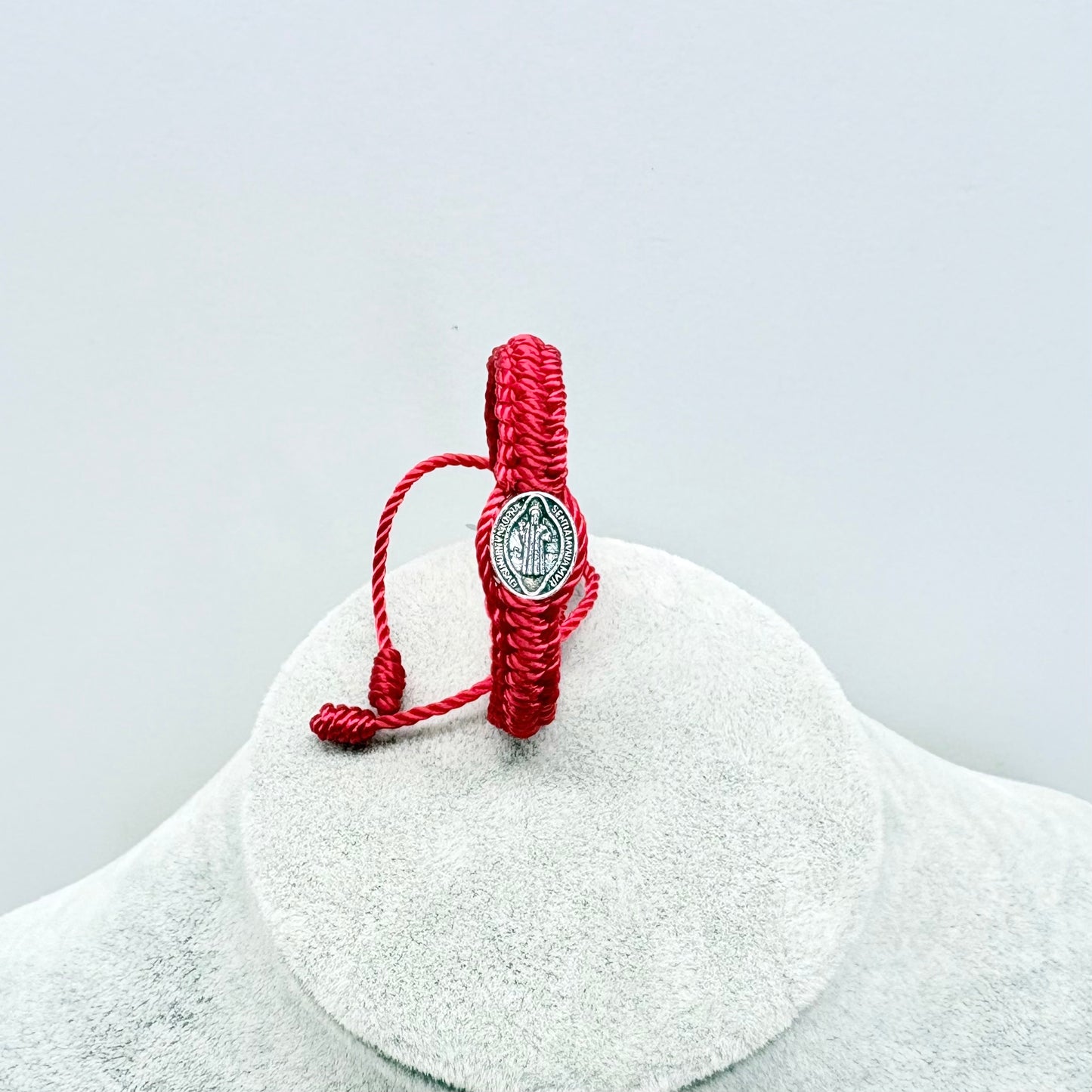 Red St Benedict baby bracelet adjustable nylon cord shown upright on display stand Catholic infant jewelry detail view