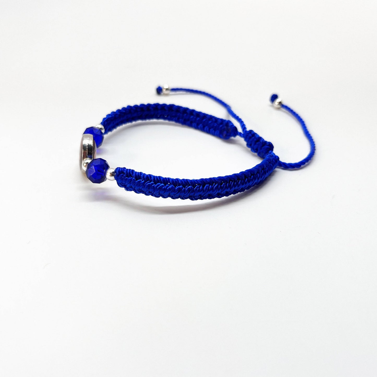 Side view of a adjustable Catholic bracelet in blue nylon thread featuring rhinestones, silver beads, and Guadalupe charm on a white background.