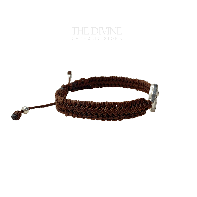 Side view of a adjustable brown nylon St. Benedict bracelet with woven cord and silver medal, durable and lightweight on a white background.