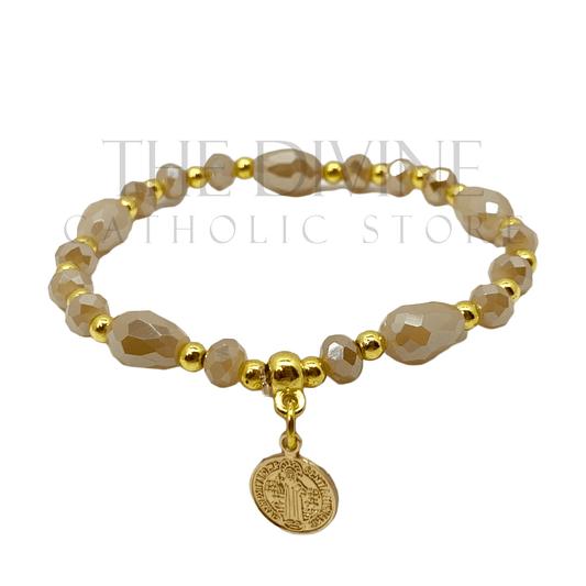 Front view of Beige and gold beaded St. Benedict bracelet with elastic band on white background.