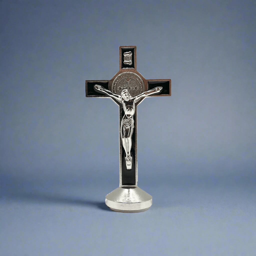 This 3 inch dashboard St. Benedict crucifix is black with a silver St.Benedict medal behind a silver corpus, silver-tone detailing and sturdy base with adhesive at bottom, with blue background.