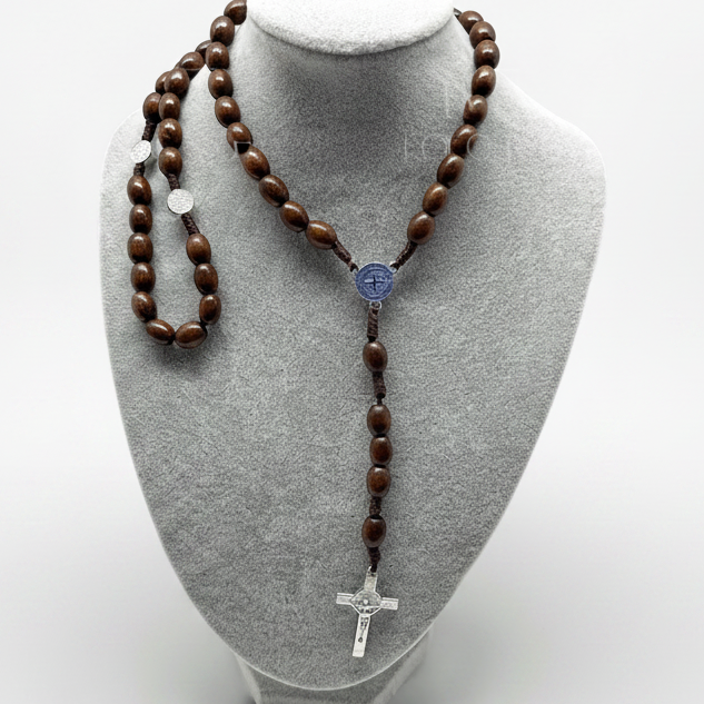 St. Benedict wooden rosary displayed on gray jewelry bust, 19-inch Catholic prayer beads with St. Benedict crucifix on a white background and surrounded by orange tulips for decoration.