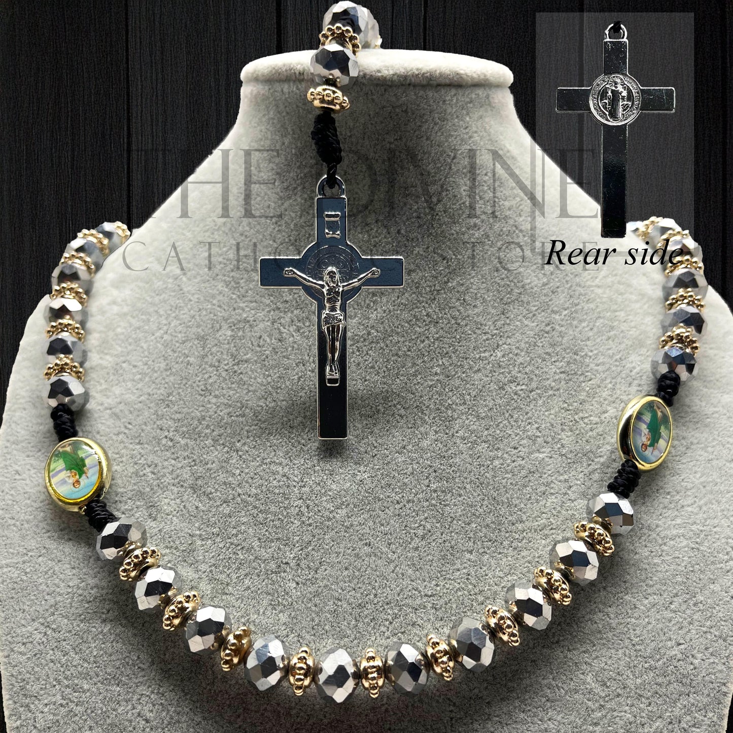 Close up of a catholic silver beaded rosary with St. Jude pendant and St. Benedict crucifix displayed on gray jewelry bust, black background.