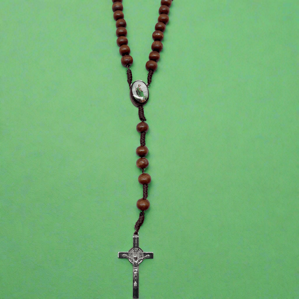 Close-up of St. Benedict crucifix pendant on wooden St Jude rosary, Catholic devotional beads on a green background.