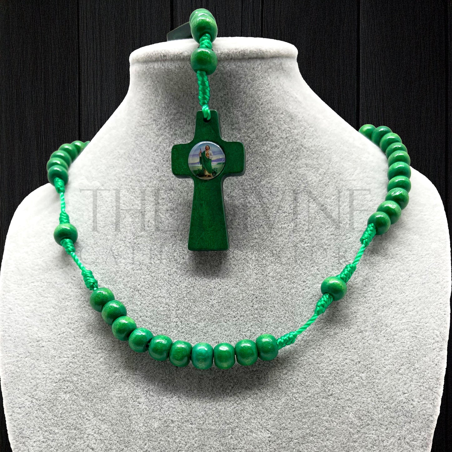 Close up of a handmade St. Jude rosary with green beads presented on jewelry bust for display on a dark backdrop.