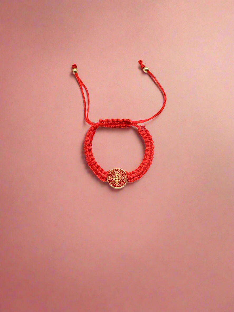 Red  St. Benedict baby bracelet braided bracelet with a circular St. Benedict medal charm on a red background.