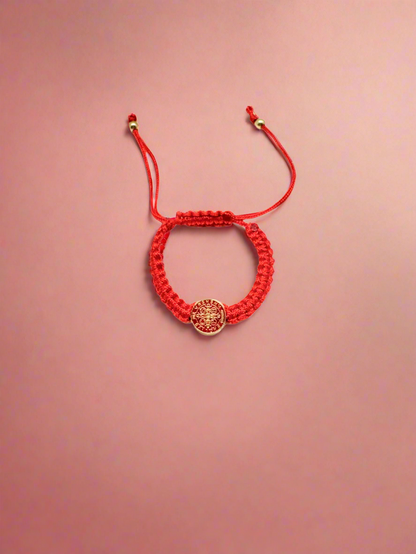 Red  St. Benedict baby bracelet braided bracelet with a circular St. Benedict medal charm on a red background.
