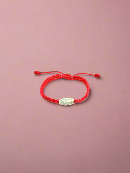 Front view of adjustable red braided baby bracelet with silver Our Lady of Guadalupe charm and silver beads, fits infants 0–12 months on a pink background