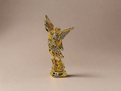 Front view of small gold colored Saint Michael Figurine on light gold background 