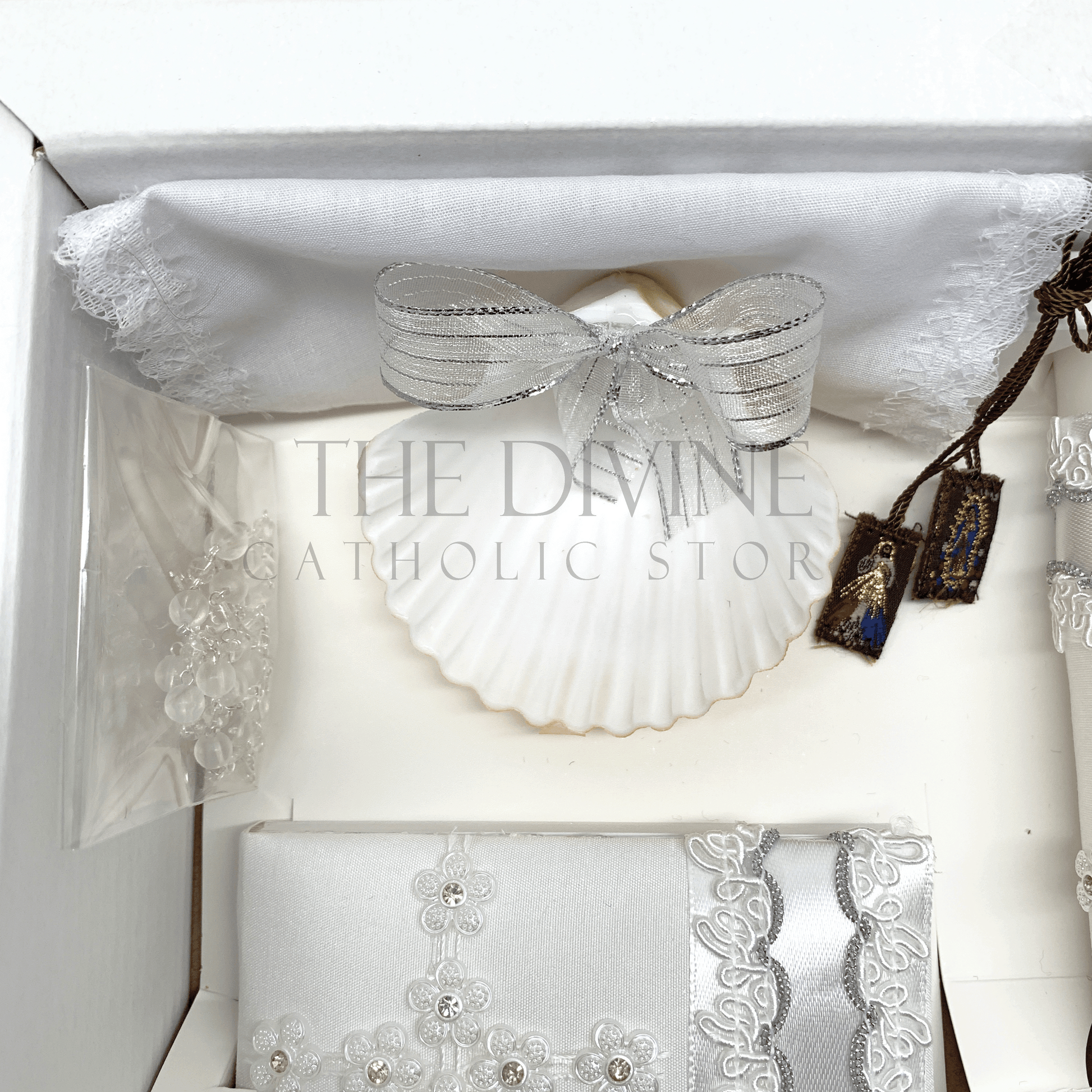 Close up image of the 6 piece baptism candle set showing white candle, shell with white ribbon, white crystal beaded rosary, and bible covered in fabric with nylon thread embroidered, and scapular with Divine Mercy and Our Lady of Guadalupe image, and fabric towel. 