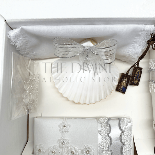 Close up image of the 6 piece baptism candle set showing white candle, shell with white ribbon, white crystal beaded rosary, and bible covered in fabric with nylon thread embroidered, and scapular with Divine Mercy and Our Lady of Guadalupe image, and fabric towel. 
