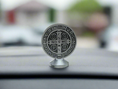 Silver St. Benedict dashboard medal placed on car dashboard for Catholic protection.