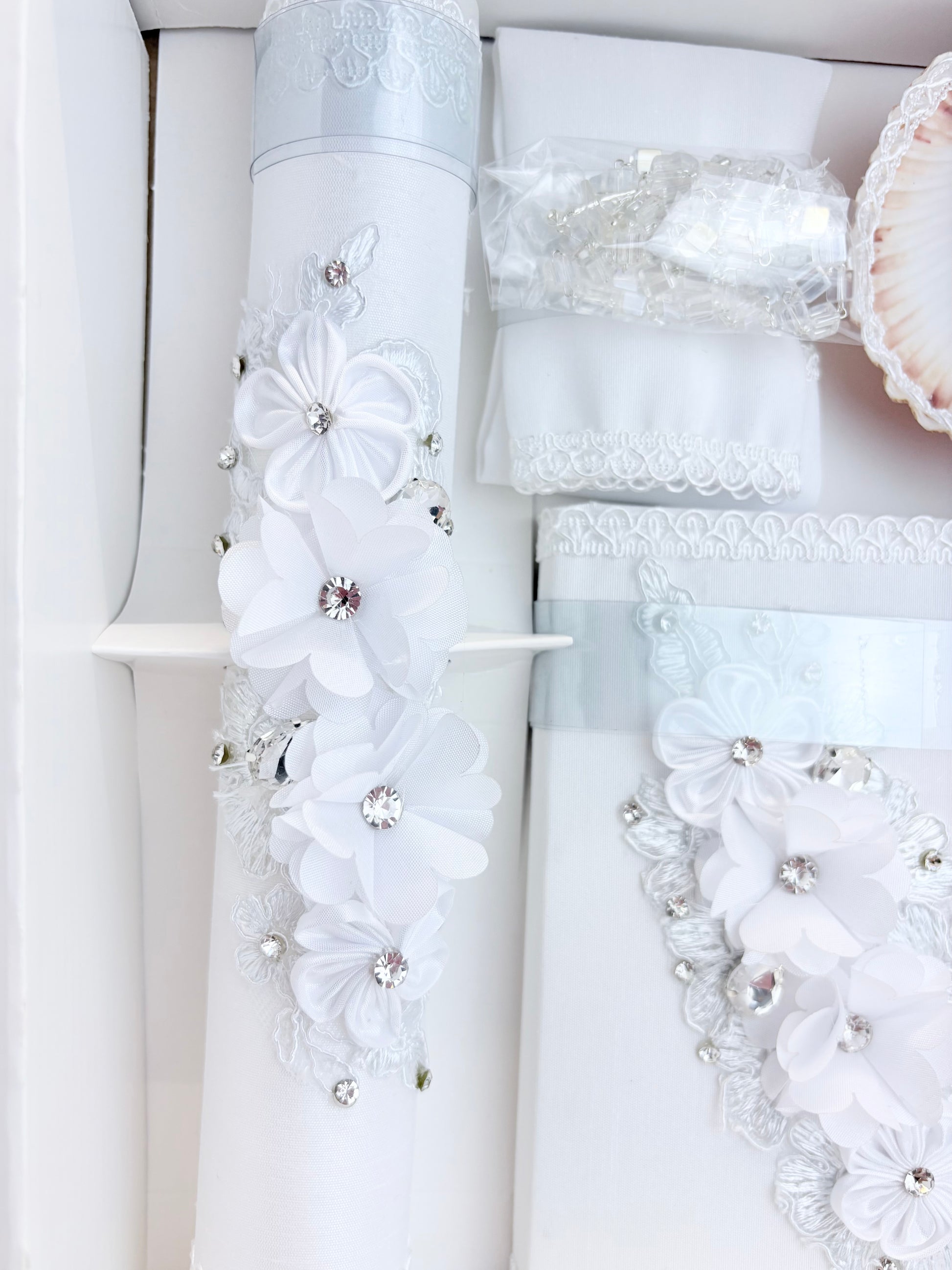 Closeup of white baptism candle and bible with cascading white chiffon flowers individual rhinestone centers and silver lace trim