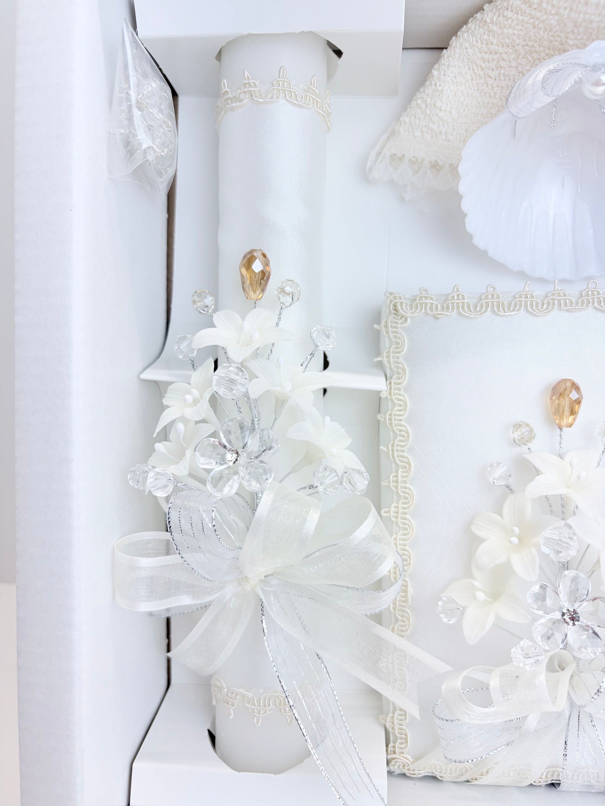 Closeup of ivory baptism candle and bible with matching crystal floral spray gold teardrop accent and organza bow