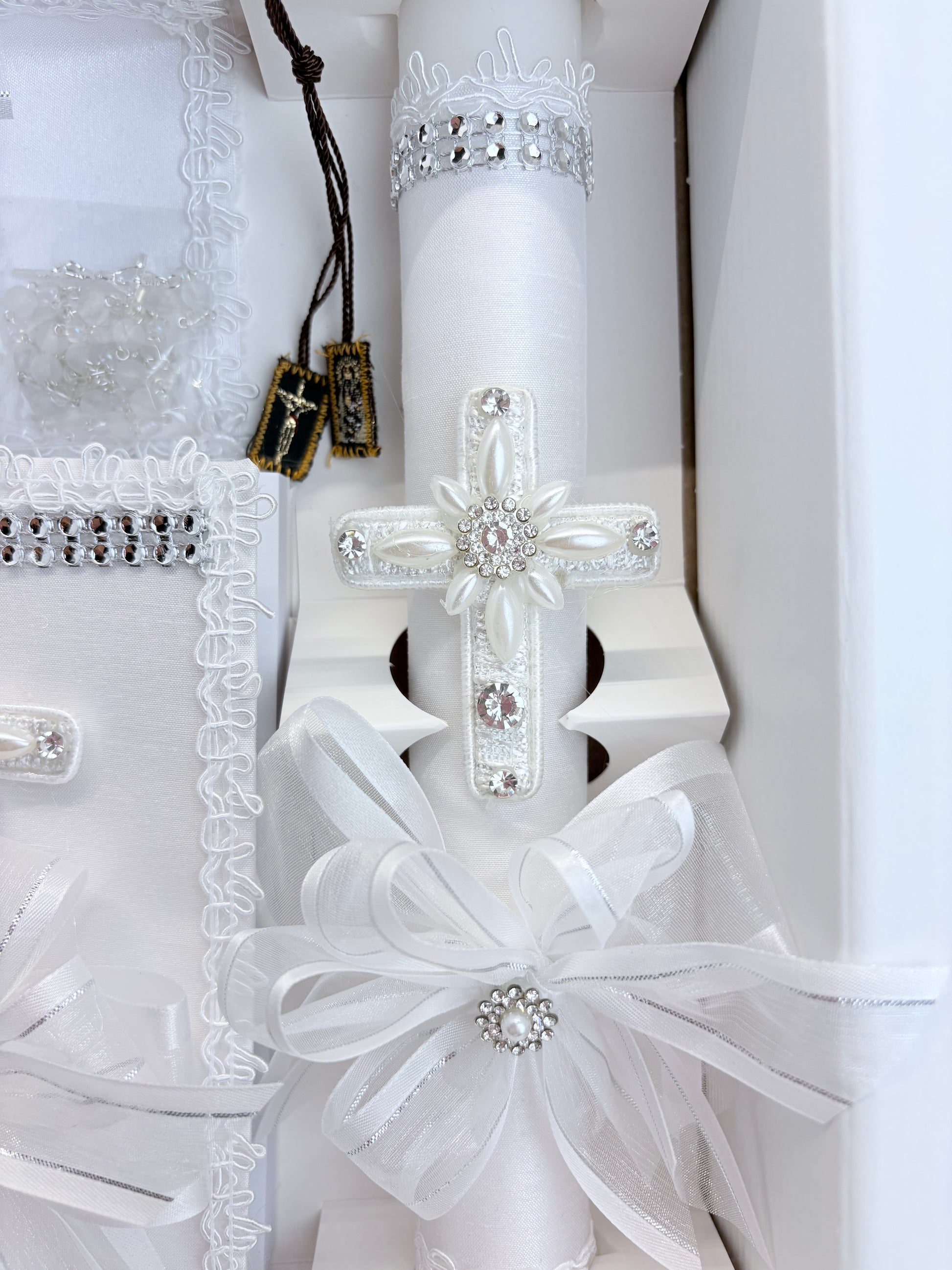 Closeup of white baptism candle with pearl cross rhinestone accents and organza bow