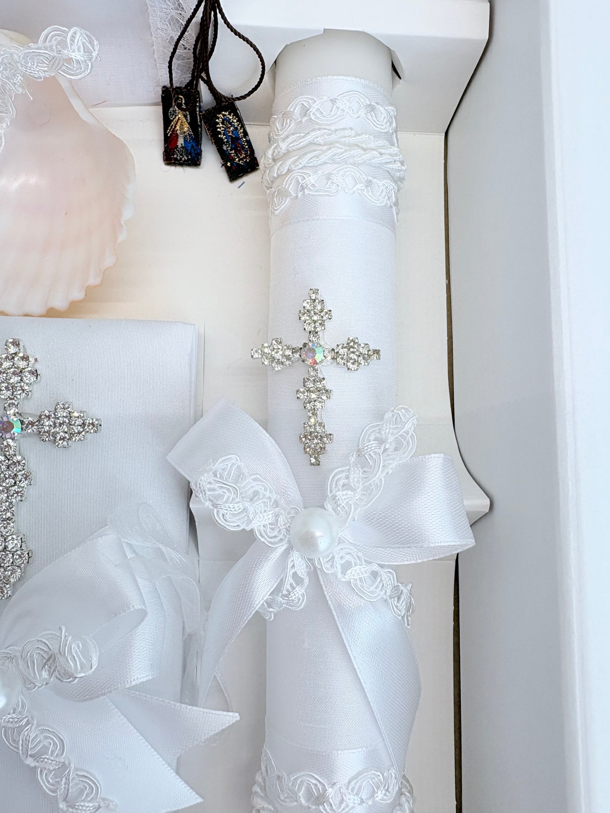 Closeup of sparkling rhinestone cross brooch with aurora borealis crystal center on white baptism candle with pearl bow