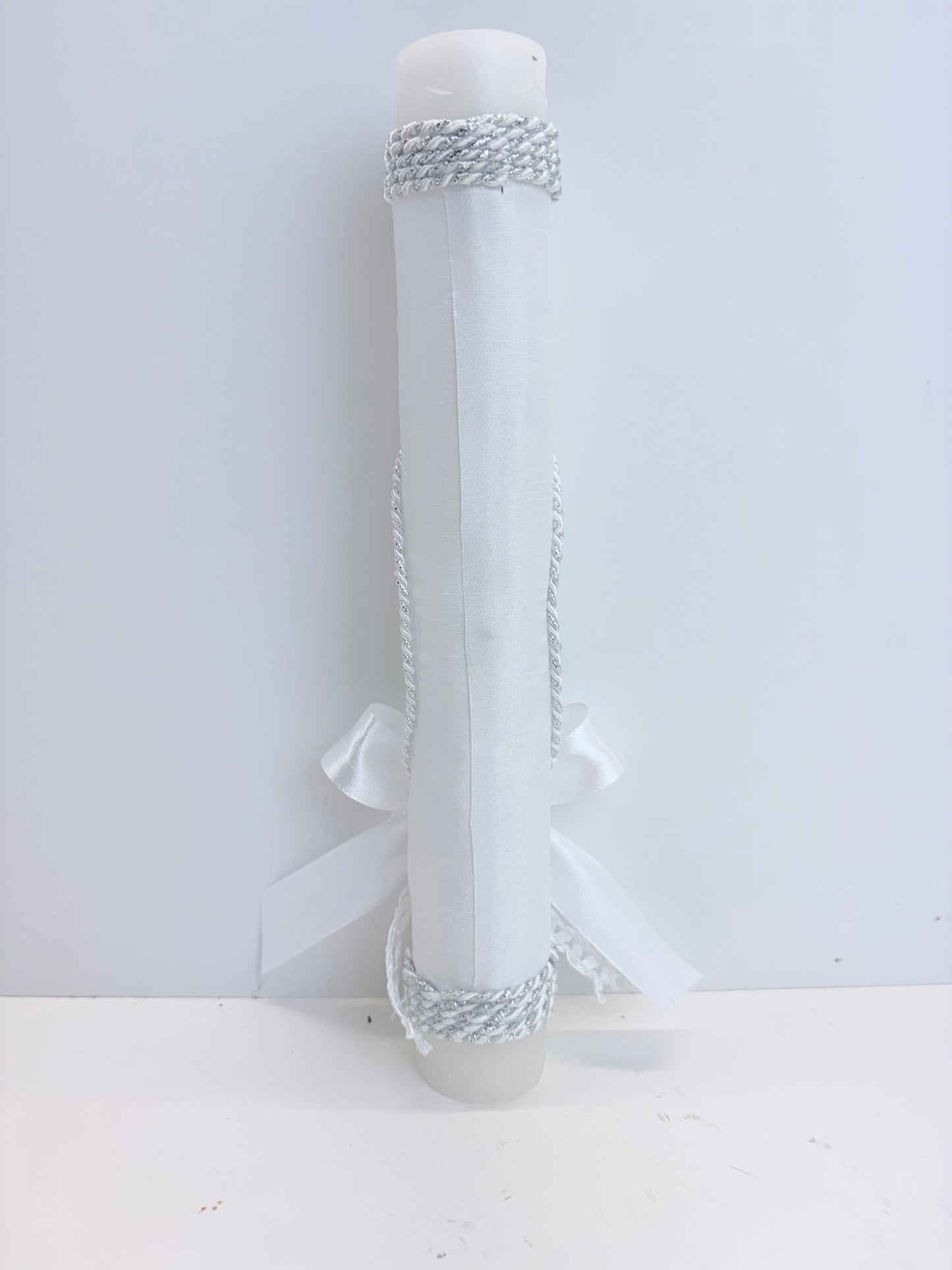 Back view of white baptism candle with silver rope trim wrap and satin bow