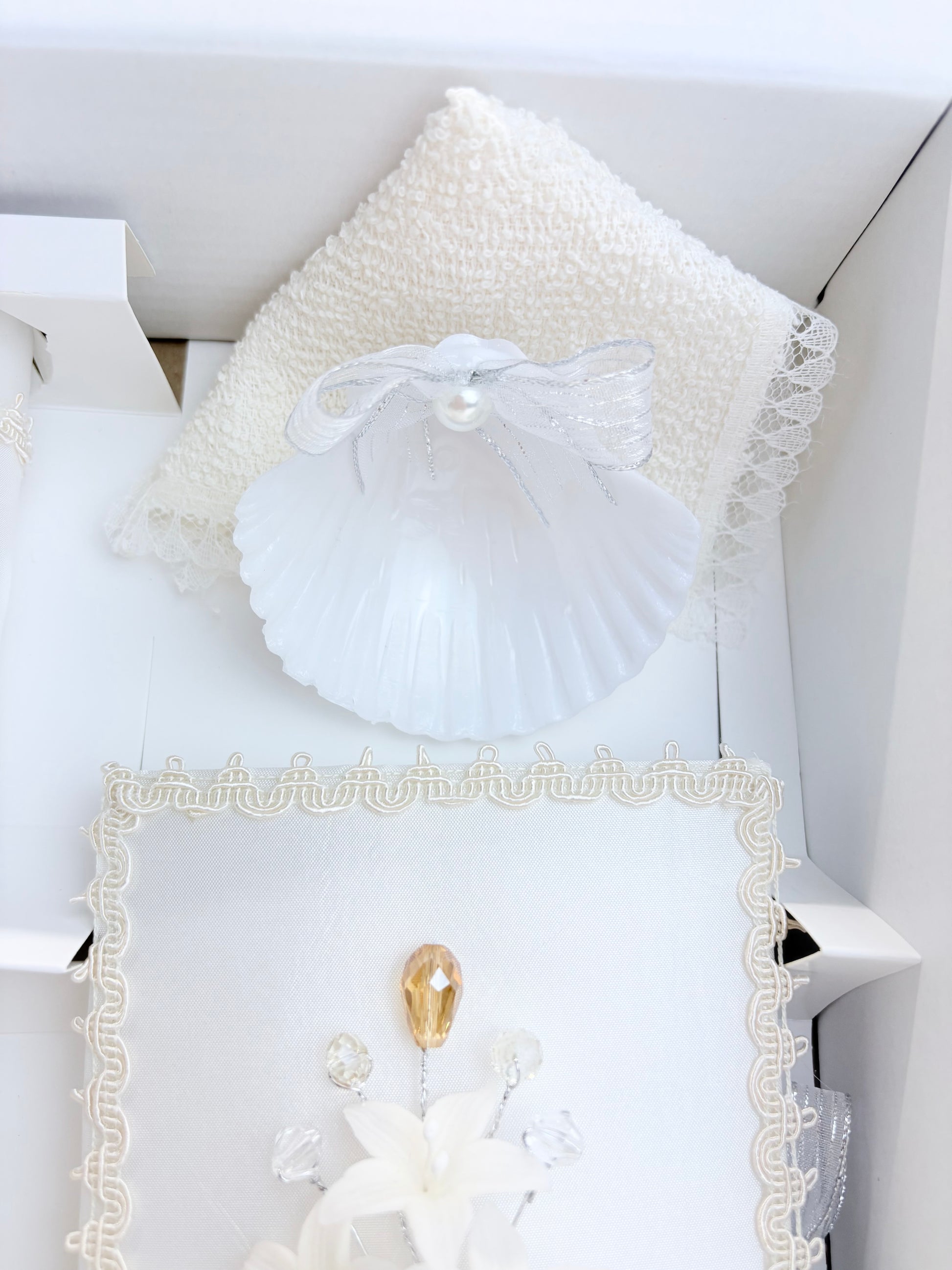 White baptism shell with pearl and silver ribbon bow and ivory textured towel handkerchief with lace trim