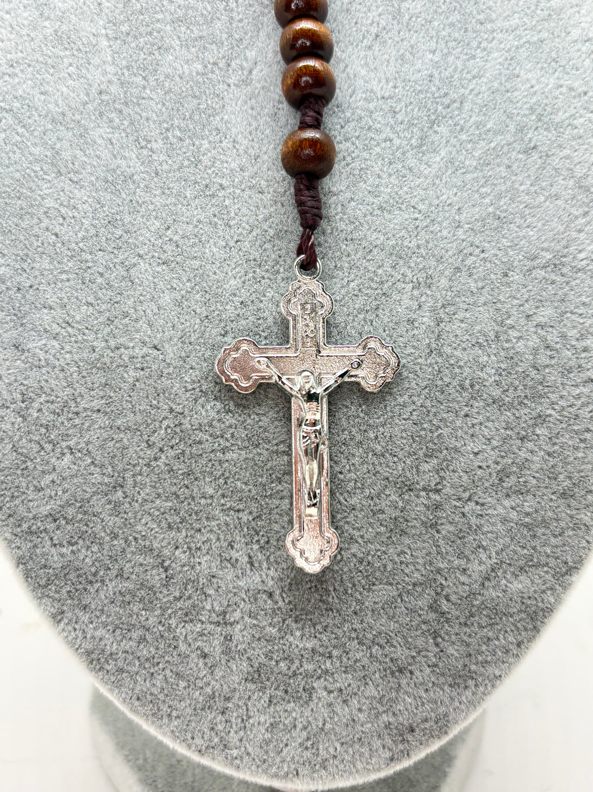 Close-up of silver crucifix on Guadalupe rosary with brown wooden beads and dark nylon cord