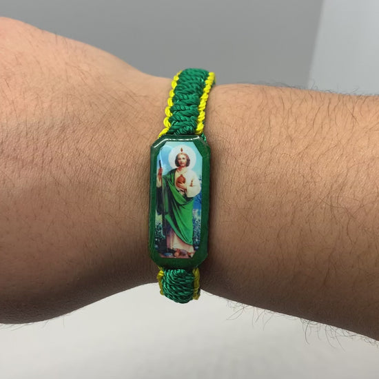 Handcrafted St. Jude bracelet featuring a green cord, yellow bead accents, and a protective St. Jude charm being modeled on a modeled wrist.