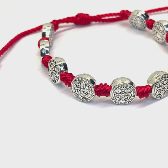 Video of a of a St. Benedict 10 Medal red cord bracelet with oxidized silver accents, adjustable size on a white background.