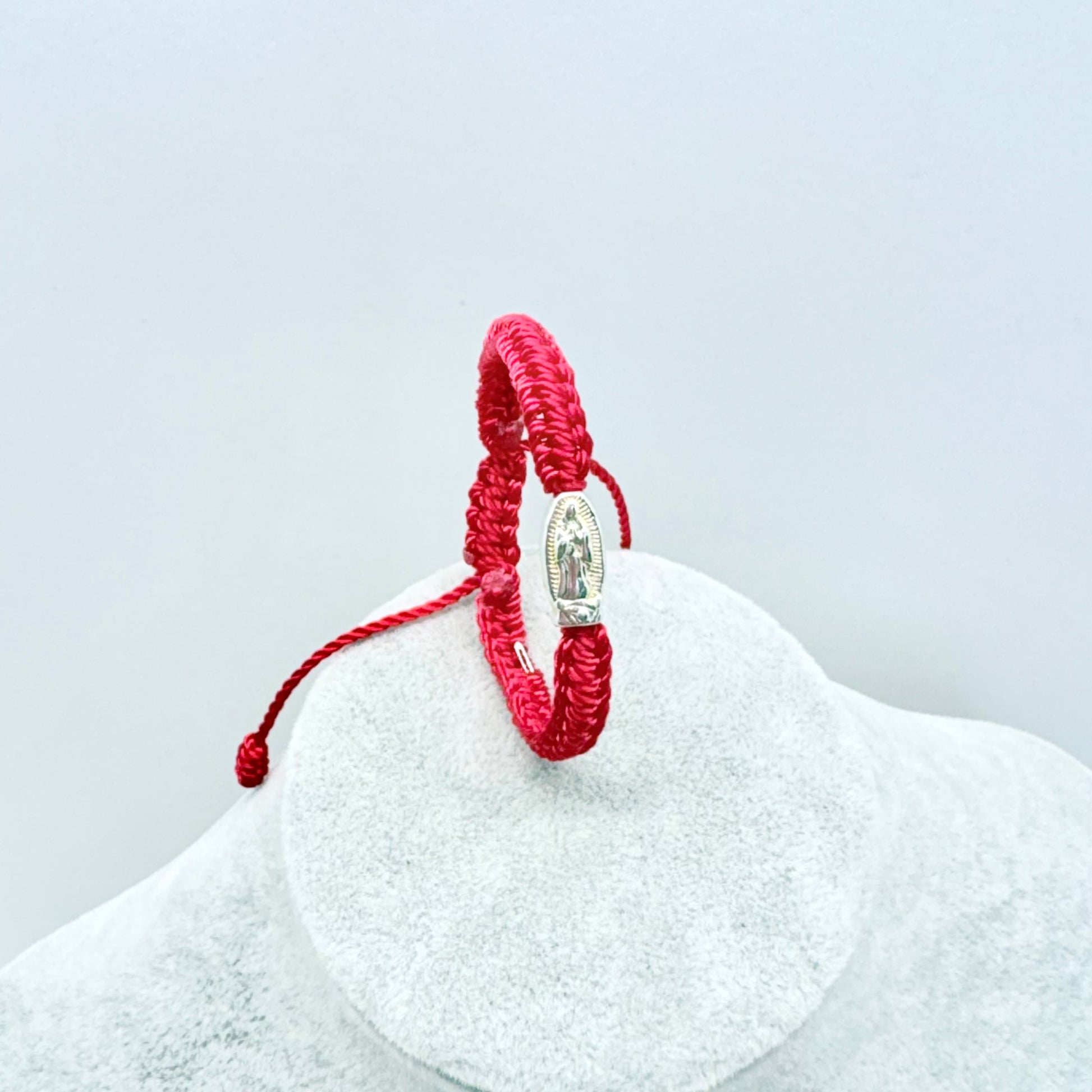 Red adjustable baby bracelet with Our Lady of Guadalupe medal shown upright on display stand, Catholic infant jewelry detail view