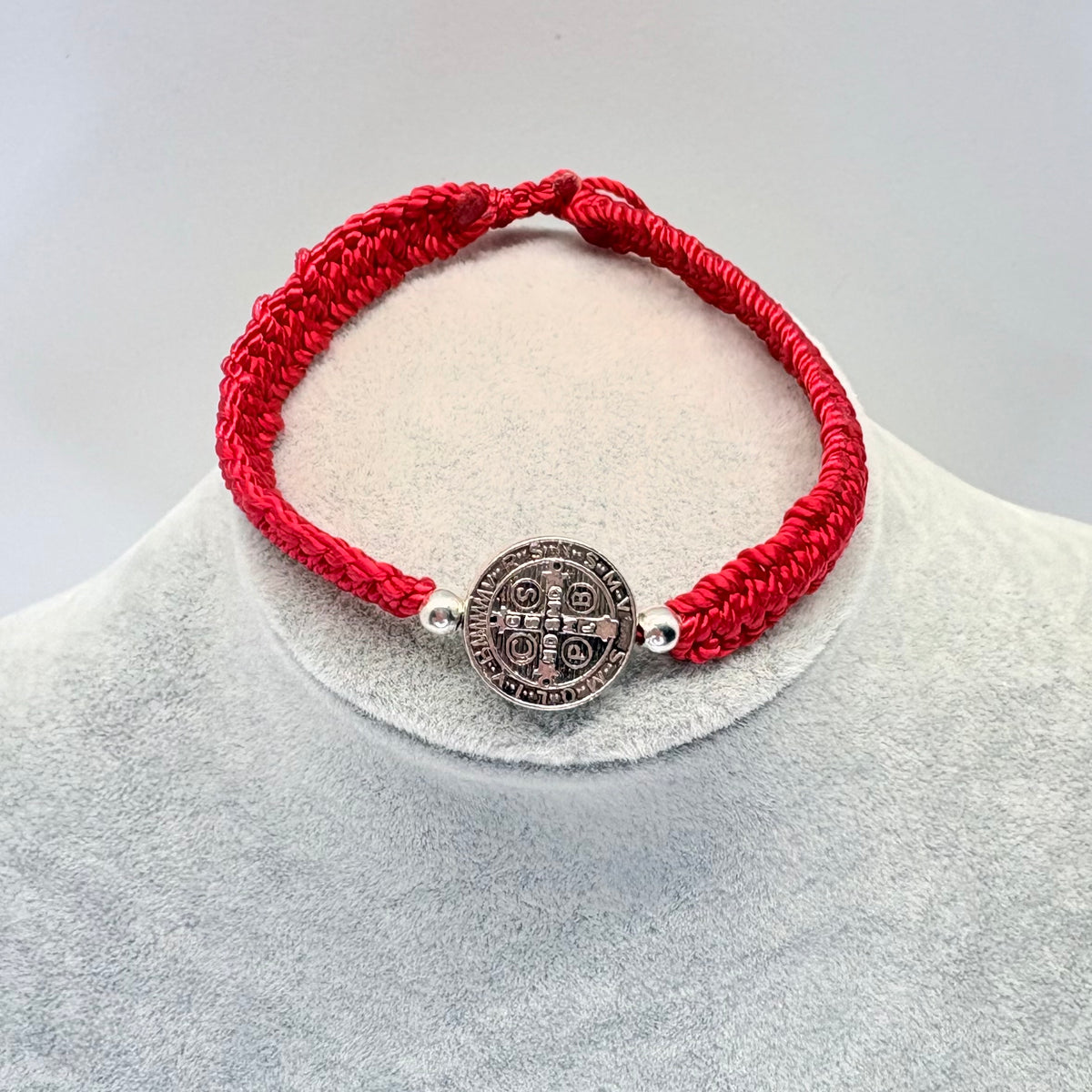 Red St. Benedict bracelet with silver beads on display stand, adjustable nylon Catholic bracelet