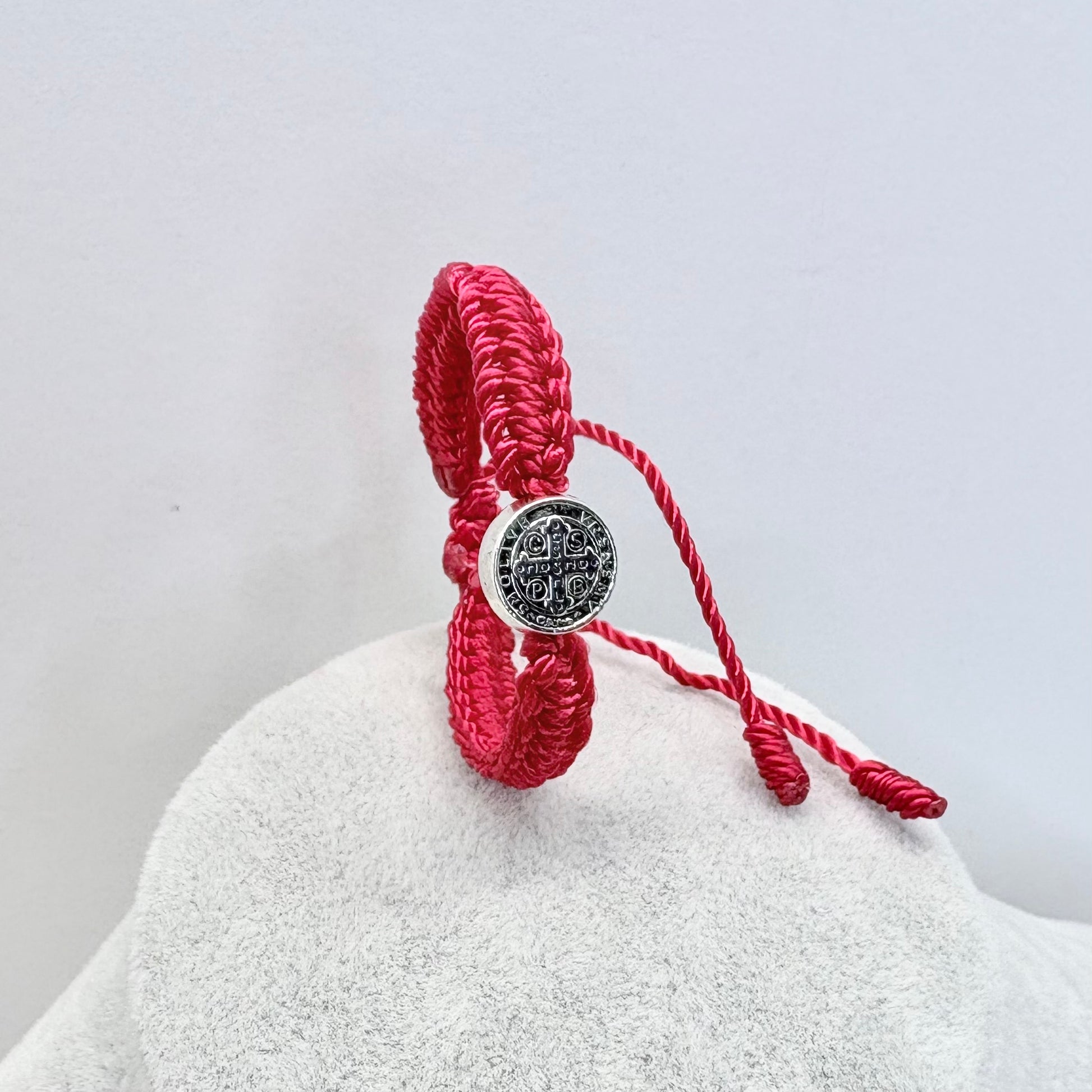 Red St. Benedict baby bracelet displayed on jewelry stand showing thickness and woven design
