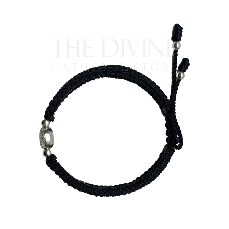 Flat lay of adjustable black nylon St Benedict bracelet showing woven cord and medal detail
