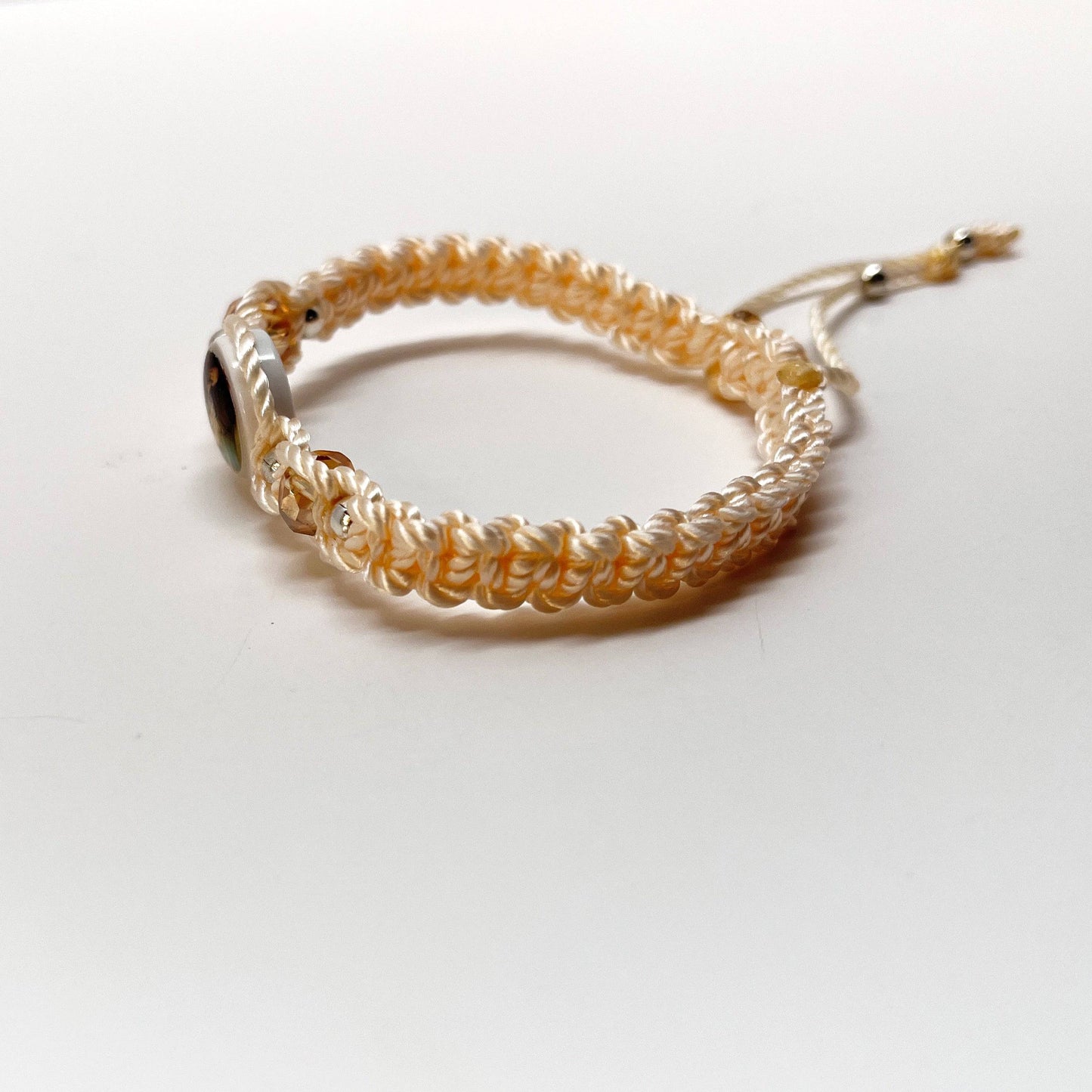 Threaded and woven beige St. Benedict bracelet with St. Benedict charm, beige crystal beads and silver-tone accents for elegant spiritual protection, side view.