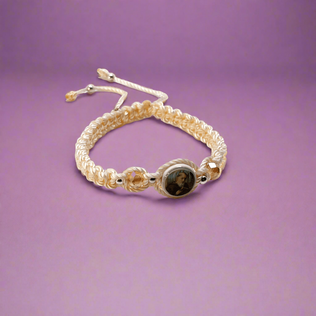 Threaded and woven beige St. Benedict bracelet with St. Benedict charm, beige crystal beads and silver-tone accents for elegant spiritual protection, with purple background.