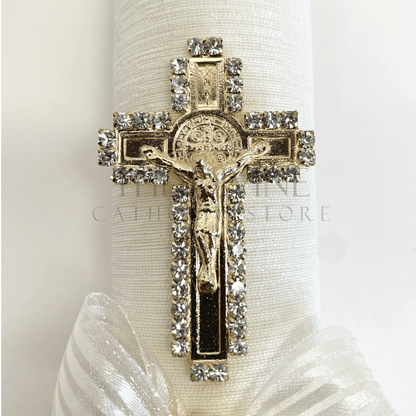 Close up view of single baptism candle decoration, gold colored St. Benedict crucifix, outlined in rhinestones.