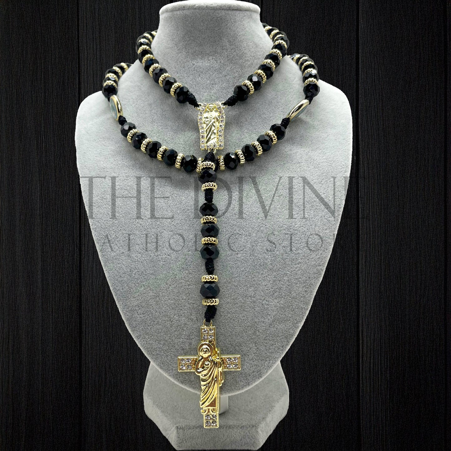 Our Crystal St. Jude rosary in black on a velvet gray bust showing details of the black crystal beads, gold colored charms in between, and gold colored St. Jude pendant and cross with rhinestones. 