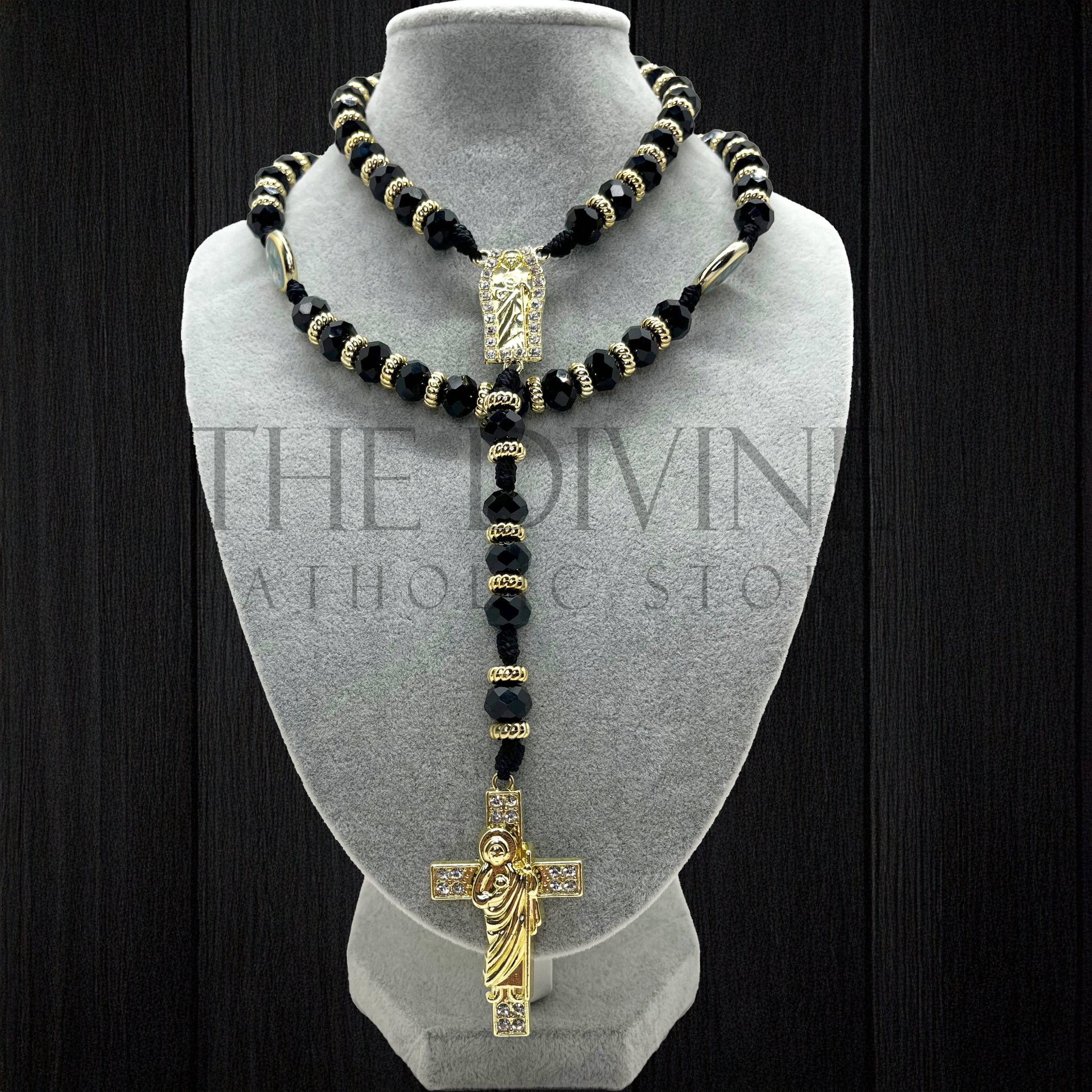 Our Crystal St. Jude rosary in black on a velvet gray bust showing details of the black crystal beads, gold colored charms in between, and gold colored St. Jude pendant and cross with rhinestones. 