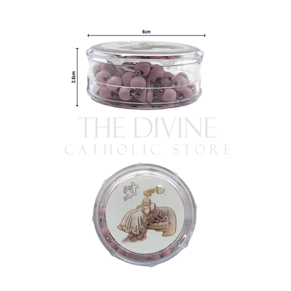 Pink baby girl baptism rosary with crucifix in round clear case featuring a baptism-themed illustration on the lid and showing dimensions of round container, 6cm x2.5 cm on white background.