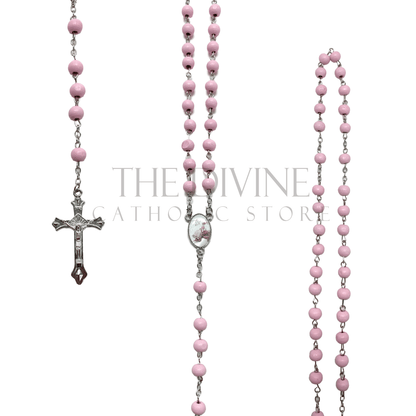 View of pink baptism rosary on a silver chain, pink wooden beads making up rosary, silver crucifix, and baptism themed charm in middle of rosary. 
