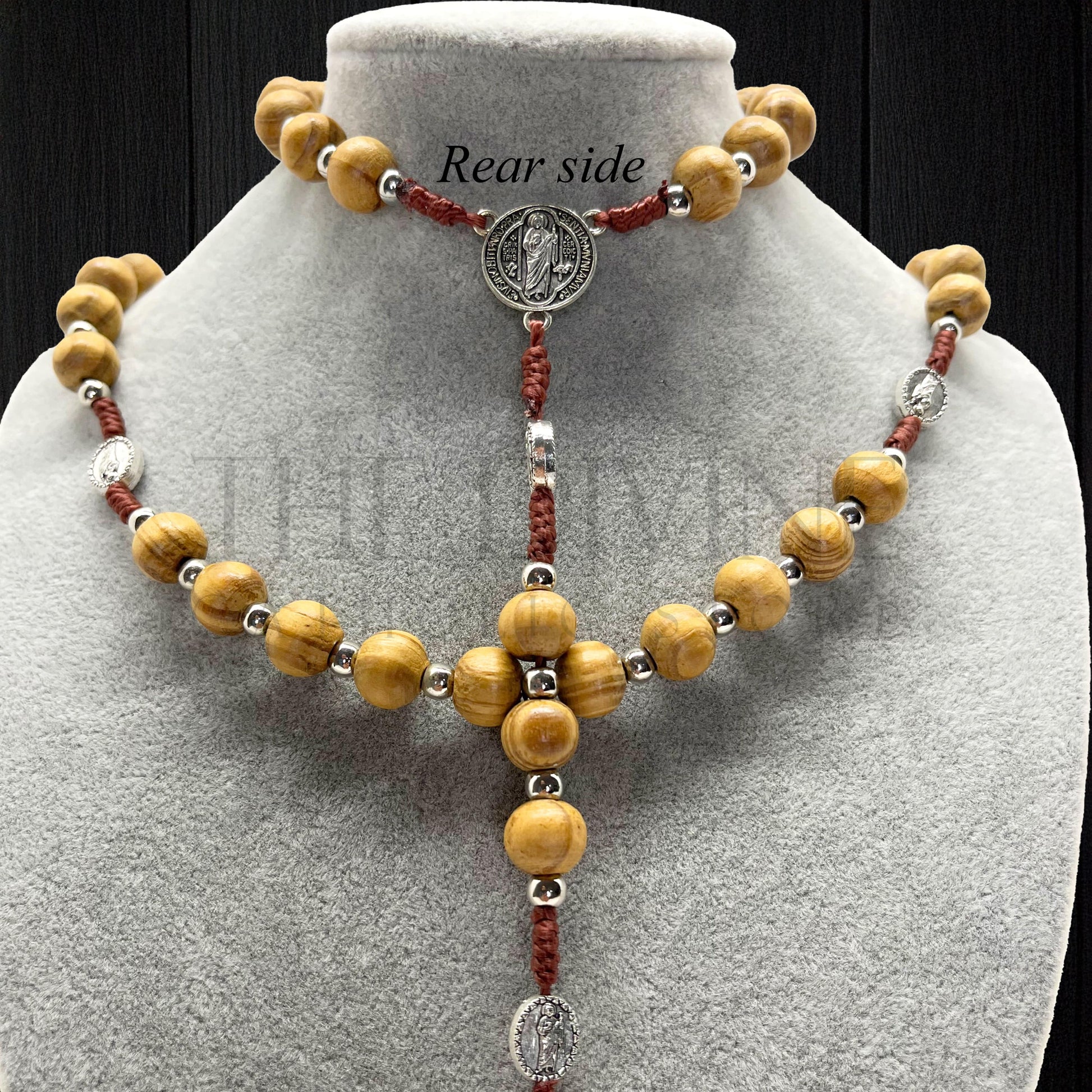 Handcrafted St. Jude and St. Benedict rosary shown on gray jewelry display stand with dark backdrop.