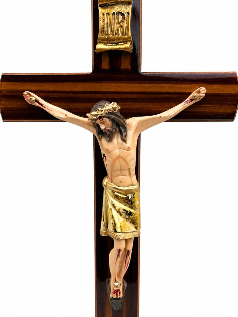 Closeup of hand painted Jesus Christ corpus with gold cloth drape crown of thorns and gold INRI embossed plaque on dark wood crucifix